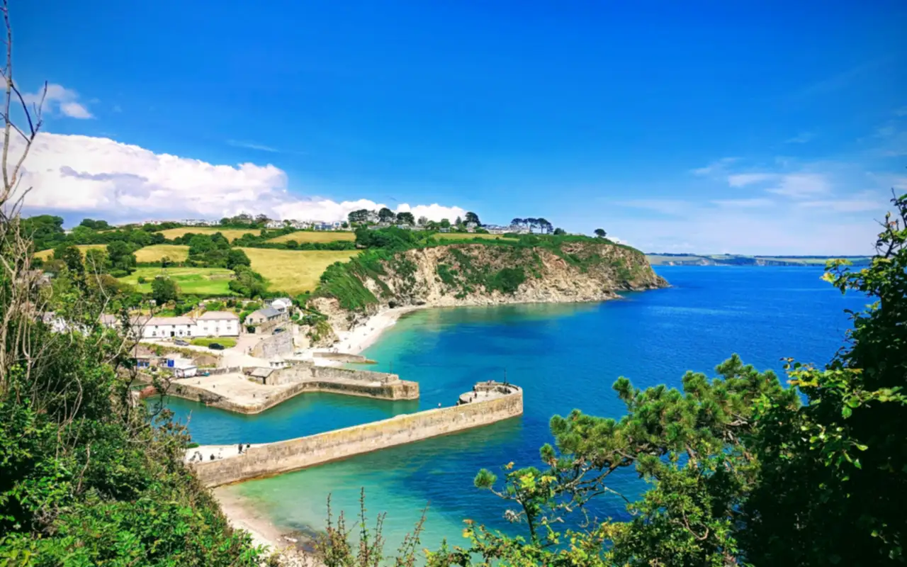 Charlestown harbour seen from the clifftop, with its harbour walls, turquoise water and the headland under a blue sky